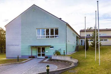 Ein modernes Gebäude mit einer blauen Fassade, weißen Fenstern und einem Weg, der zum Eingang führt. Das Gebäude hat ein Namensschild auf der linken Seite.
