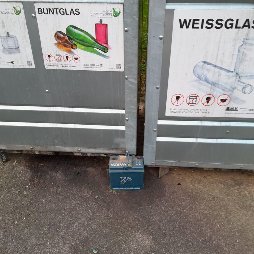 Zwei Metallbehälter zum Recycling von farbigem und klarem Glas. Unten unter den Behältern befindet sich eine Batterie.