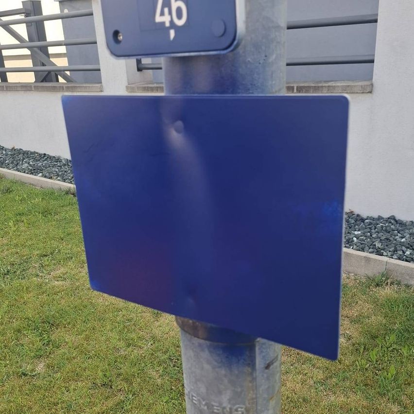 Ein blaues rechteckiges Schild mit der Nummer 46, montiert an einem Pfosten. Das Schild hat eine beschädigte Ecke.
