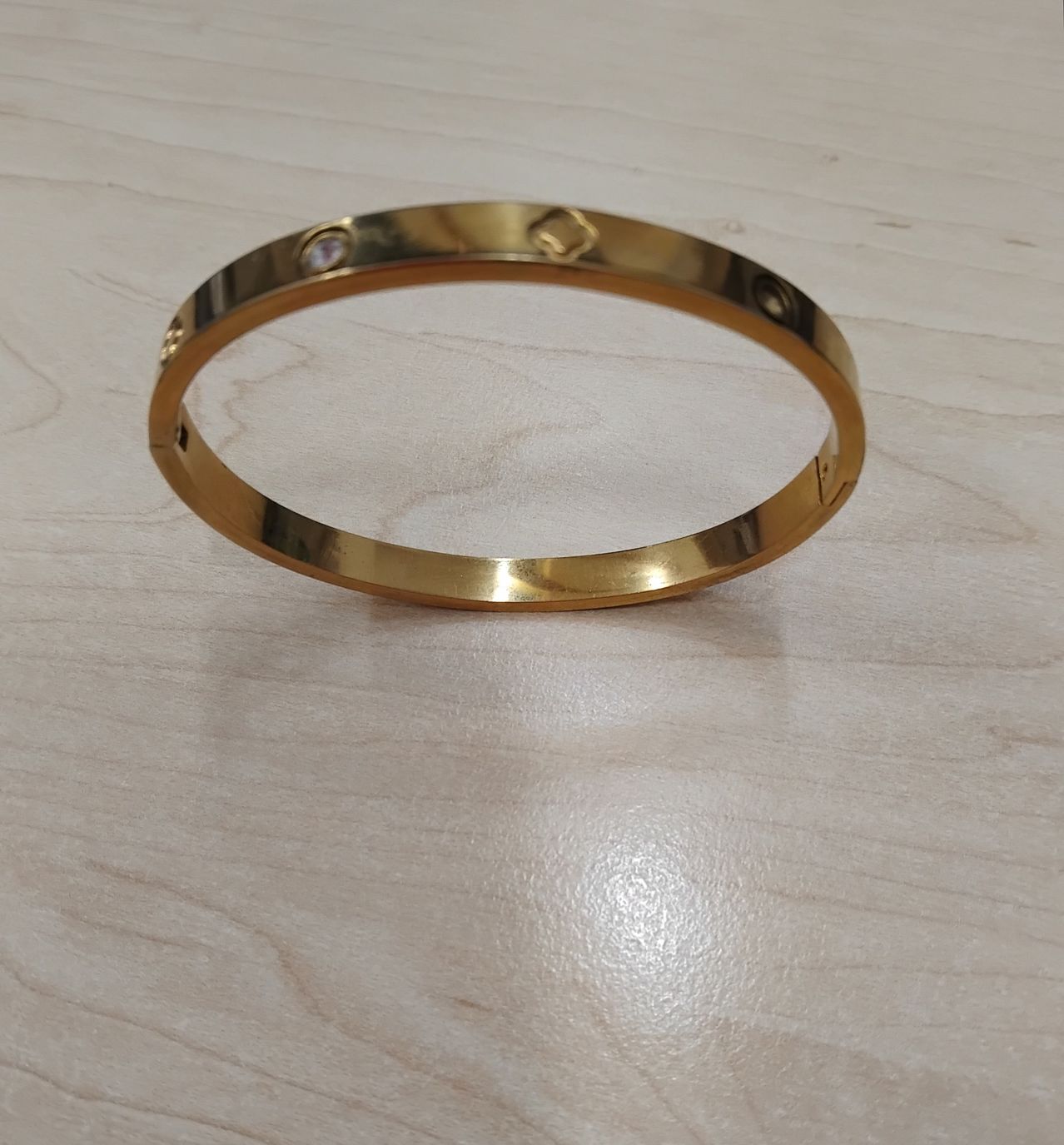 Ein vergoldetes Armreif-Armband mit einem kleinen Diamanteinlage auf einer Holzoberfläche.