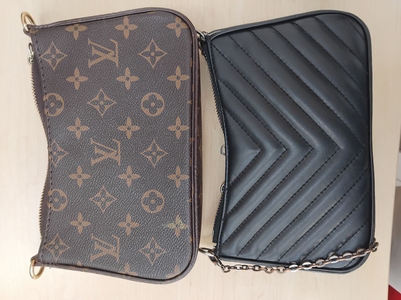 Zwei Louis Vuitton Handtaschen sind nebeneinander ausgestellt. Die linke hat ein braunes Monogrammmuster, die rechte ist schwarz mit einem Chevron-Muster. Beide haben Reißverschluss und Metallkettenriemen.