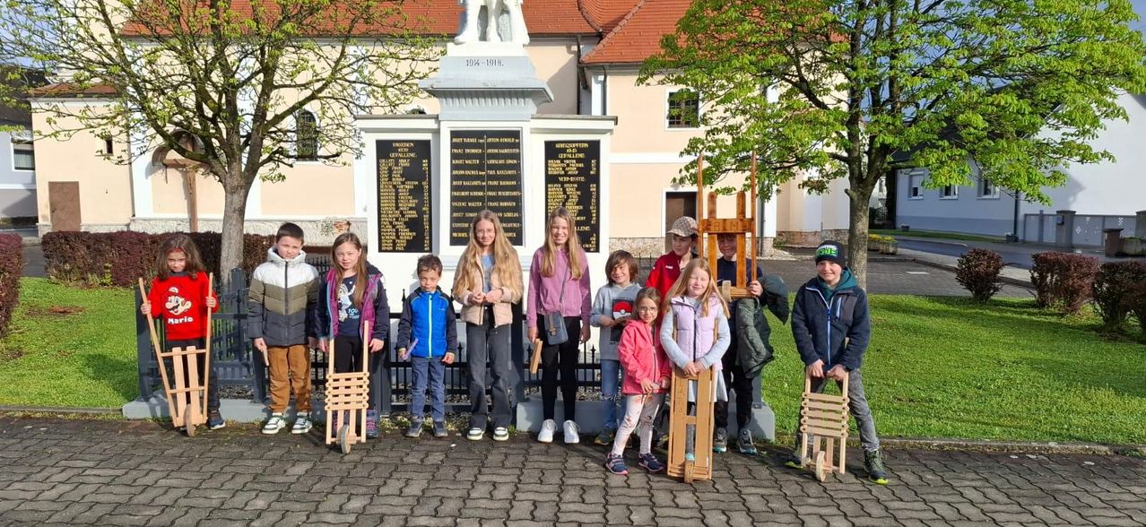 Eine Gruppe von Kindern steht vor einem Denkmal mit Holzschlitten.