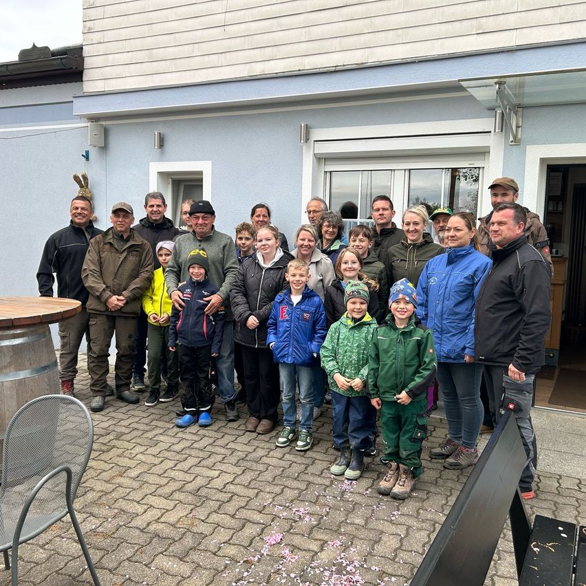 Gruppe von Erwachsenen und Kindern, darunter Jungen und Mädchen, in Winterkleidung, vor einem blauen Gebäude mit weißer Tür stehend.