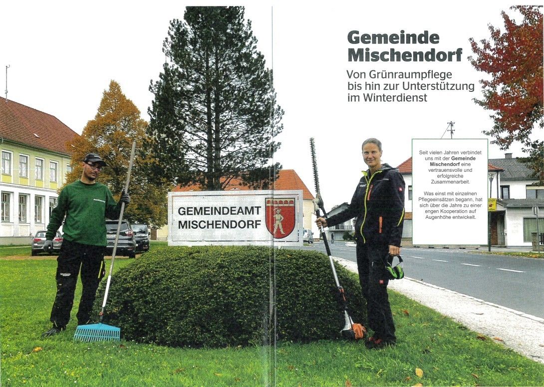 Ein Bild von zwei Personen in einem Park mit einem Schild, das Gemeinde Mischendorf liest. Eine Person hält ein Werkzeug, und die andere hält eine Harke. Hinter ihnen ist eine Hecke, und im Hintergrund sind Autos und ein Gebäude.