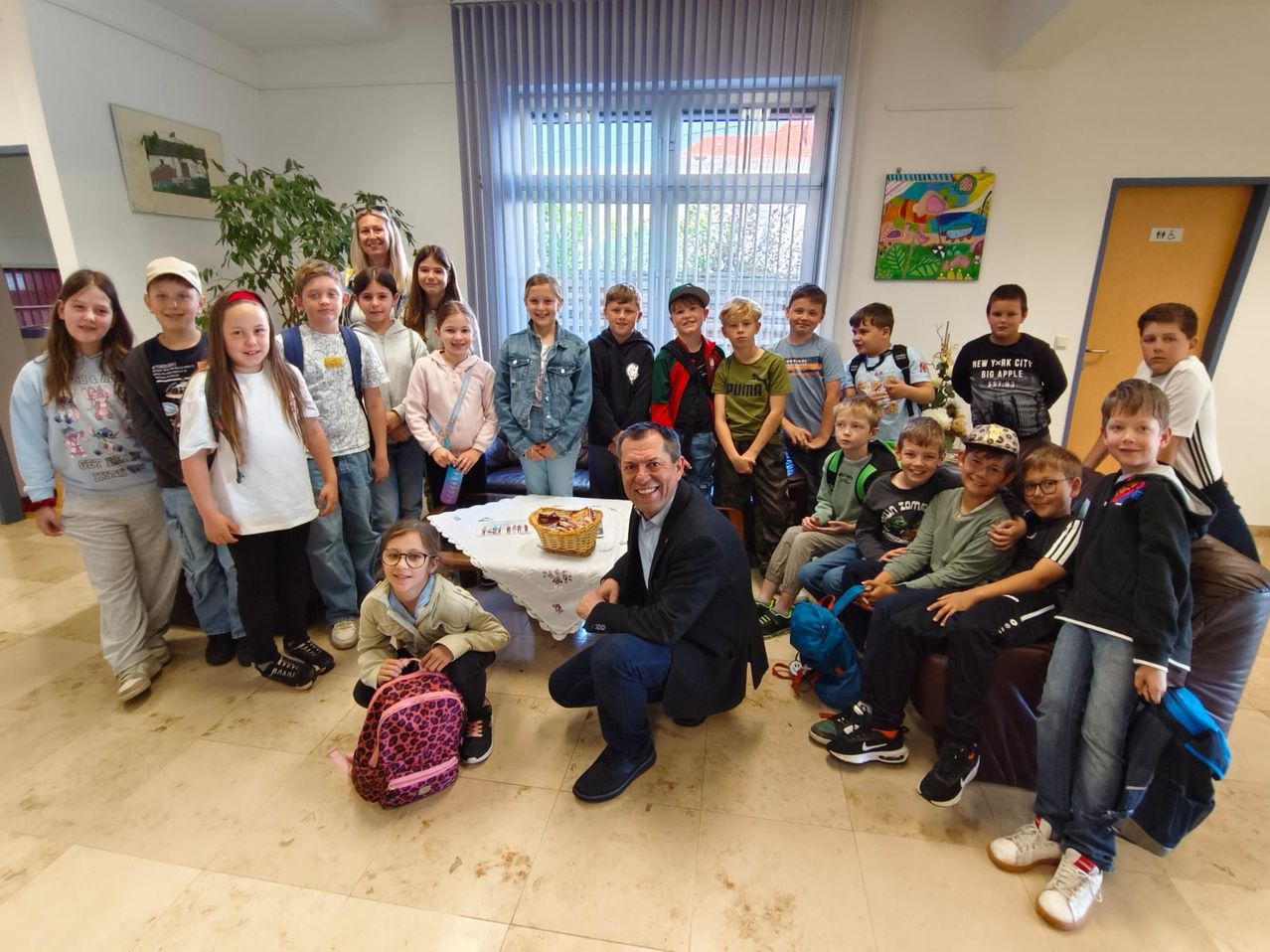 Eine Gruppe von Kindern und Erwachsenen posiert für ein Foto in einem Raum mit einem Tisch, einem Mann im Anzug und einem Korb mit Essen.