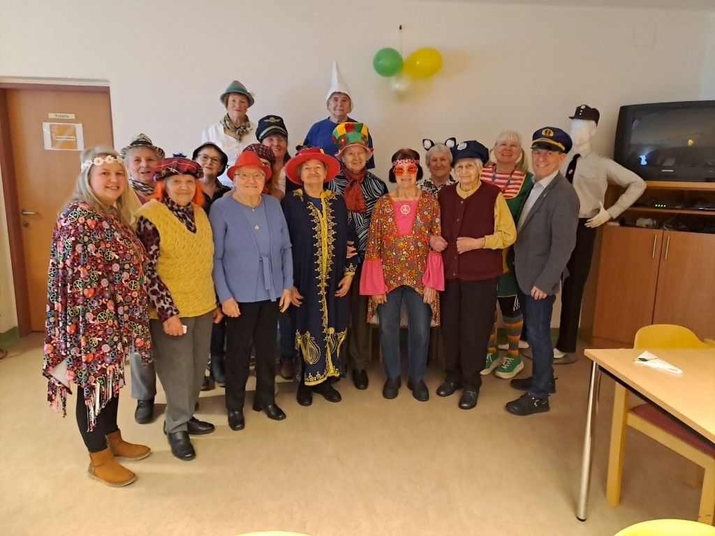 Eine Gruppe von Menschen in Hüten und farbenfrohen Kostümen posiert für ein Foto in einem Raum mit Luftballons und einer Puppe.