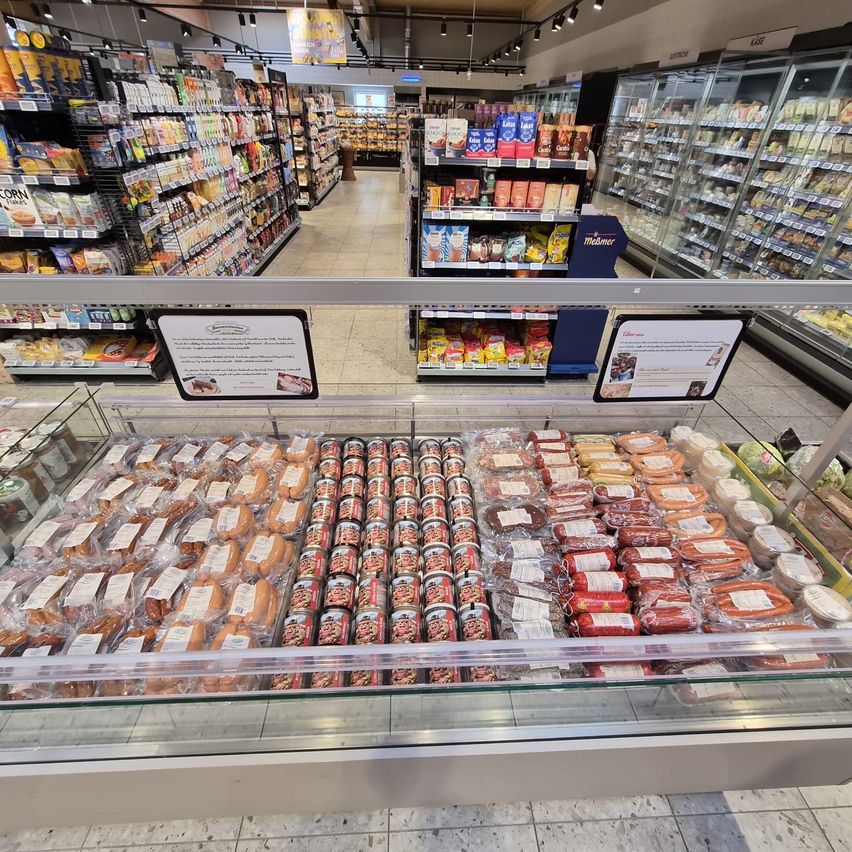 Ein Supermarkt mit verschiedenen Produkten zur Schau. Ein Glastresen hält mehrere Lebensmittel, darunter Würstchen, Würstchen in Dosen und Würstchen in Plastikverpackungen.