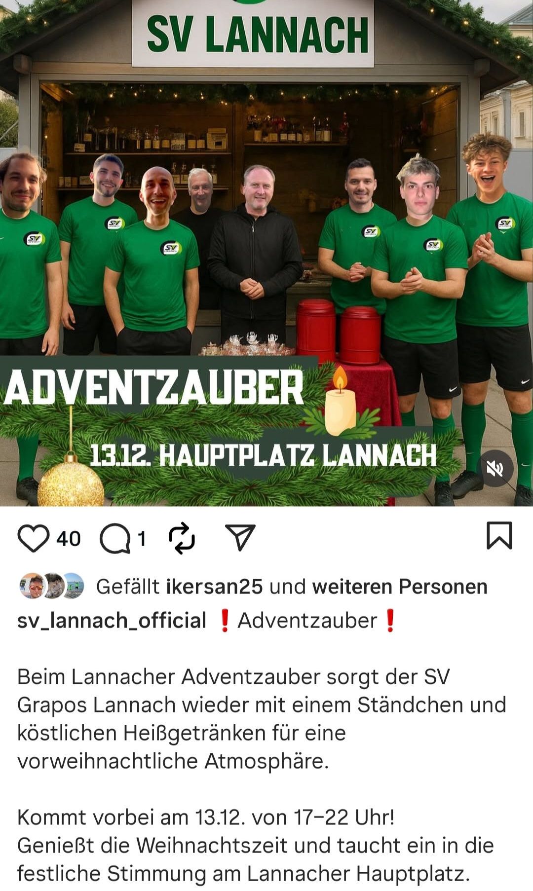 Eine Gruppe von Menschen steht vor einem festlichen Aufbau. Einige tragen grüne Trikots, andere schwarze Jacken. Ein Schild mit der Aufschrift 'ADVENTZAUBER'. Eine Kerze und eine goldene Kugel sind auf dem Tisch. Das Bild hat einen Wasserzeichen.