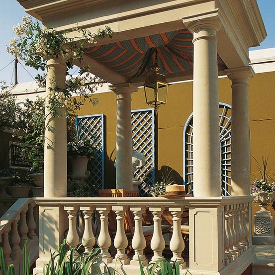 Ein Pavillon mit einem gestreiften Baldachin und beigefarbenen Säulen mit einer Brüstung und Holzstühlen.