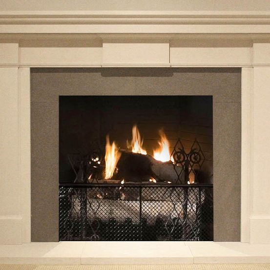 Ein weißer Kamin mit einem dekorativen Rahmen und einem schwarzen Eisengitter. Im Inneren des Kamins brennt ein Feuer, das Licht an die Wand wirft.