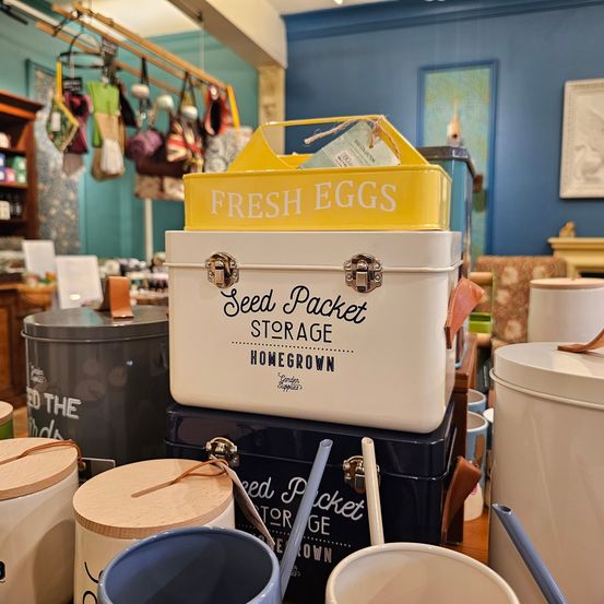 In einem Geschäft sind verschiedene Aufbewahrungsboxen angeordnet. Eine gelbe Box ist oben mit dem Wort 'Frisches Ei'. Darunter befindet sich eine weiße Box mit 'Samenpaket-Aufbewahrung'. Darunter ist eine blaue Box mit 'Samenpaket'.