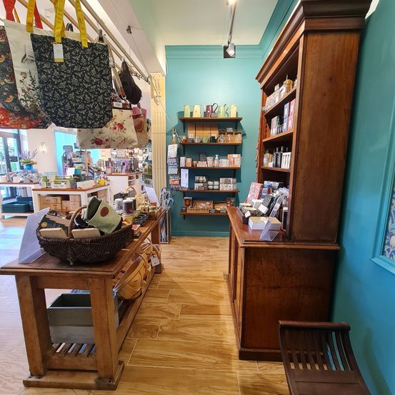 Ein Boutique mit blauen Wänden und Holzregalen, gefüllt mit Produkten. Ein Korb mit Gegenständen steht auf einem Tisch im Vordergrund.