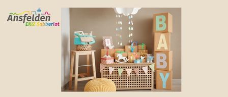 Ein Raum mit einer Babyparty-Einrichtung, bestehend aus einem Holzhocker mit einem Korb, einem Tisch mit Babygeschenken und einer Wand mit dem Wort 'BABY' aus Blöcken.