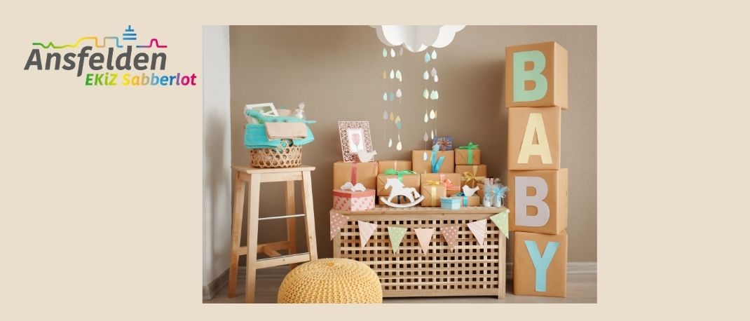 Ein Raum mit einer Babyparty-Einrichtung, bestehend aus einem Holzhocker mit einem Korb, einem Tisch mit Babygeschenken und einer Wand mit dem Wort 'BABY' aus Blöcken.