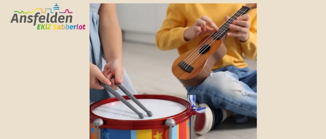 Zwei Kinder spielen Musikinstrumente. Eines hält Trommelstöcke und spielt eine Trommel, während das andere eine kleine Gitarre spielt. Das Bild hat einen Wasserzeichen mit dem Text 'Ansfelden' und 'EKiz Sabbrlo'.