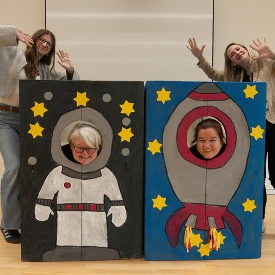Drei Frauen posieren in einem Raum, zwei in Pappaufstellern eines Raumschiffs und eines Astronauten, mit einer Frau, die hinter ihnen steht.