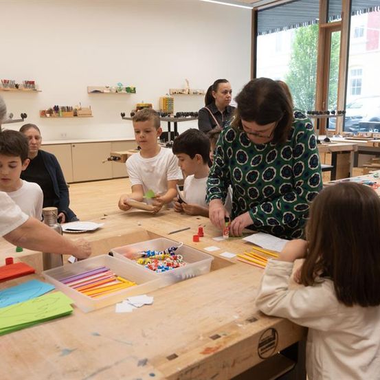 Eine Gruppe von Kindern und zwei Frauen arbeitet an einem Projekt am Tisch. Es gibt verschiedene Kunstmaterialien auf dem Tisch.
