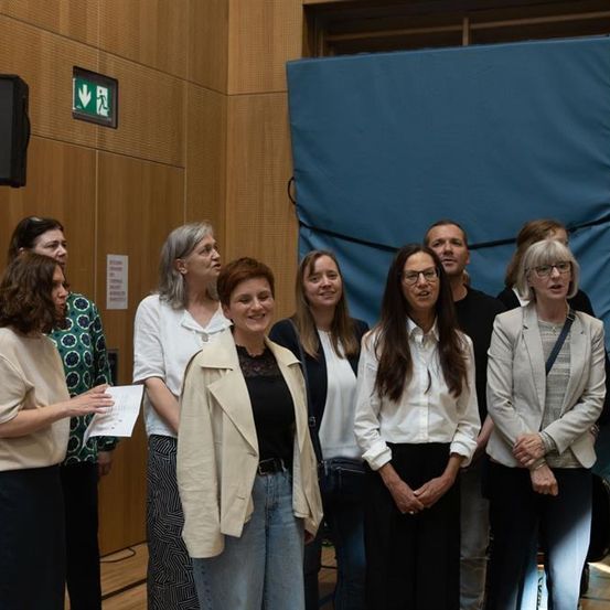 Eine Gruppe von Menschen, darunter Frauen und Männer, stehen gemeinsam in einem Raum, möglicherweise für ein Foto. Sie alle lächeln und scheinen für die Kamera zu posieren.