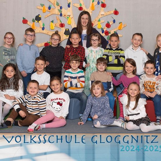 Eine Gruppenaufnahme von Schülern und einer Lehrerin an der Volksschule Gloggnitz, mit einem dekorativen Baum im Hintergrund, für das Schuljahr 2024-2025.