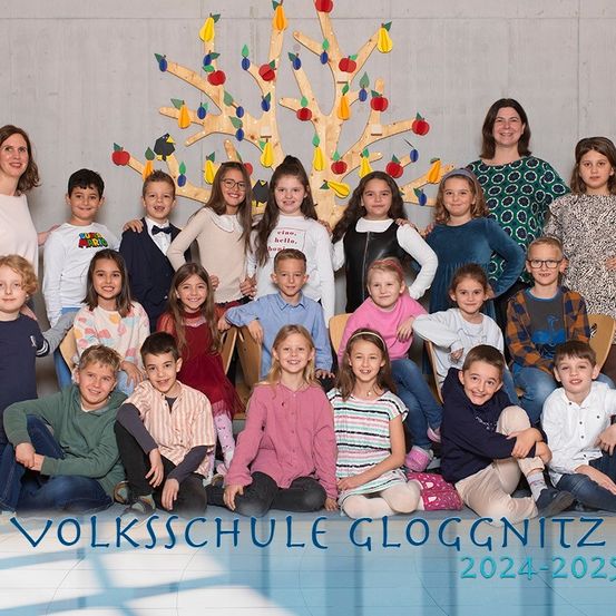 Eine Gruppenaufnahme von Schülern und Lehrern an der Volksschule Gloggnitzer, vor einem geschmückten Baum, für das Schuljahr 2024-2025.