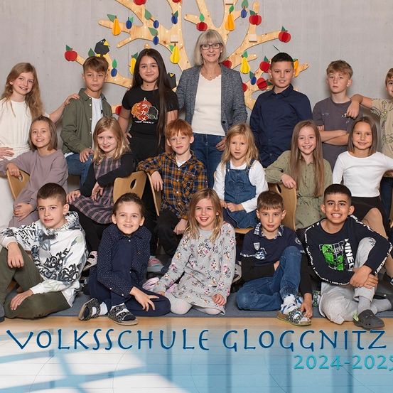 Ein Gruppenfoto von Schülern und einer Lehrerin an der Volksschule Gloggnitz für das Schuljahr 2024-2025. Die Schüler sitzen auf Stühlen, während die Lehrerin hinter ihnen steht.