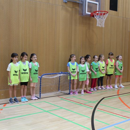 Eine Gruppe junger Mädchen in passenden gelben Uniformen mit dem Wort 'erima' darauf stehen in einer Reihe auf einem Basketballplatz.