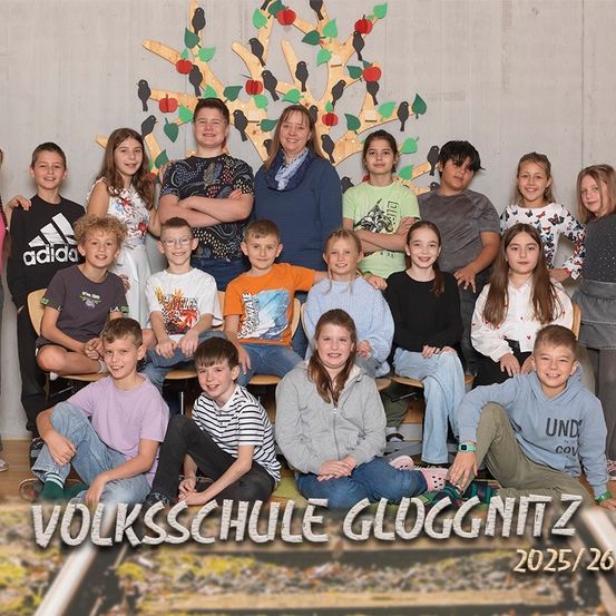 Gruppenfoto von Schülern und einer Lehrerin an der Volksschule Gloggnitzer. Die Lehrerin steht in der Mitte, mit mehreren Schülern, die um sie herum sitzen und stehen. Das Foto wurde 2025/26 aufgenommen.