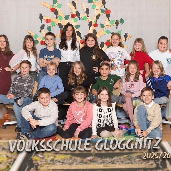 Eine Gruppe von Schülern und einer Frau sitzen zusammen vor einem Baumhintergrund mit Äpfeln und Vögeln. Sie lächeln für ein Klassenfoto.
