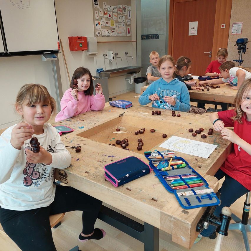 Eine Gruppe junger Mädchen sitzt an einem Holztisch in einem Klassenzimmer und arbeitet an einem Projekt mit Nüssen und einem Stiftetui.