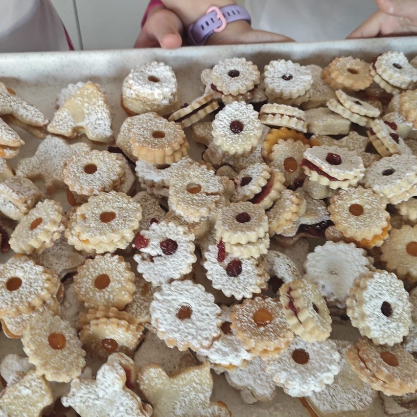 Ein Tablett gefüllt mit einer Vielzahl von Keksen. Viele von ihnen sind mit Puderzucker bestreut und haben Füllungen wie Marmelade und Mandeln. Einige Kekse haben verschiedene Formen wie Herzen, Sterne und Tiere.