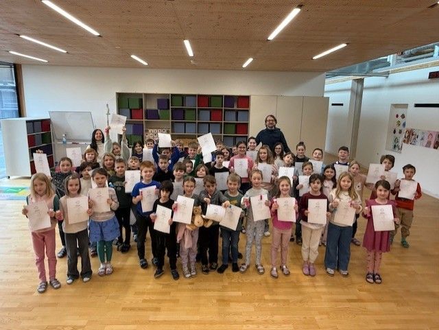Eine Gruppe von Kindern, die Zertifikate in einem Klassenzimmer halten, mit einem Lehrer, der hinter ihnen steht.
