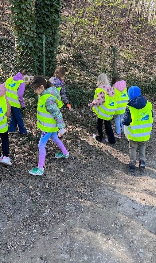 Eine Gruppe von Kindern in Neonwesten sammele Müll auf einem Feldweg. Sie tragen Handschuhe und Sneakers.
