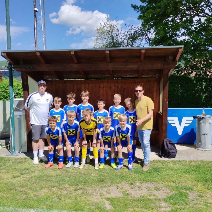 Eine Jugendfußballmannschaft posiert für ein Foto vor einer Schutzhütte mit zwei Erwachsenen.