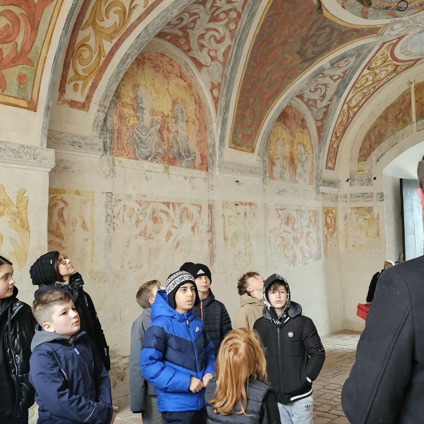 Eine Gruppe von Kindern und Erwachsenen steht in einem kunstvoll verzierten Raum mit Fresken an den Wänden und der Decke.