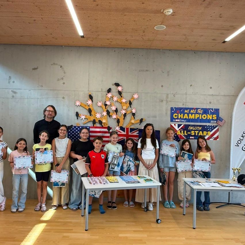 Eine Gruppe von Kindern und Erwachsenen steht vor einer Wand mit verschiedenen Dekorationen und hält Urkunden in der Hand, um ein Foto zu machen.