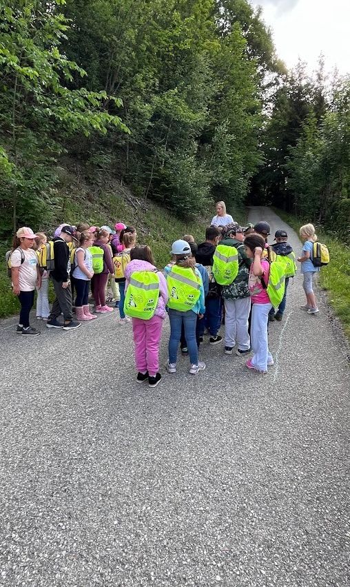 Eine Gruppe von Kindern mit reflektierenden Westen läuft auf einem Schotterweg, angeführt von einer Frau.