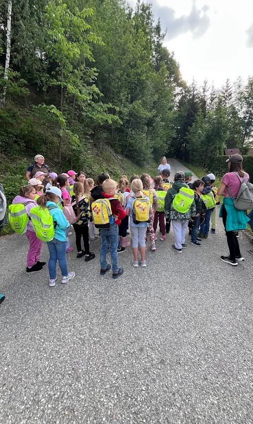 Eine Gruppe von Kindern mit Rucksäcken steht am Straßenrand, wahrscheinlich in einem Wald.
