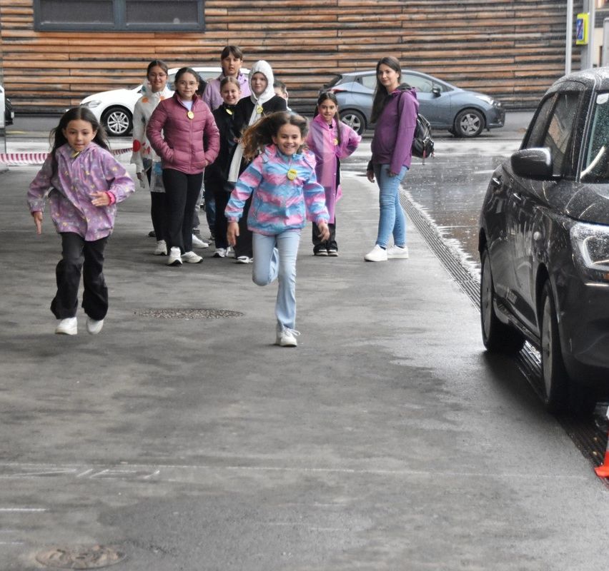Eine Gruppe junger Mädchen, einige in Jacken und Turnschuhen, rennt auf einem nassen Bürgersteig. Ein Auto ist am Straßenrand geparkt.