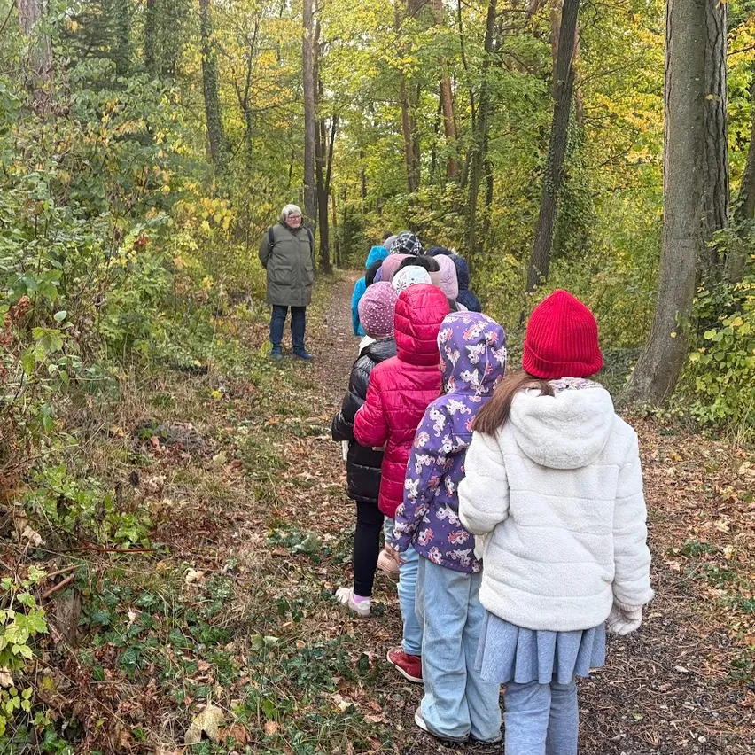 Eine Gruppe von Kindern, einige mit Mützen und Jacken, gehen auf einem Waldweg.