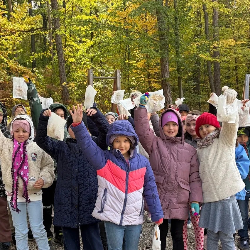 Eine Gruppe von Kindern in Winterkleidung posiert für ein Foto im Wald und hält weiße Papiere in den Händen.