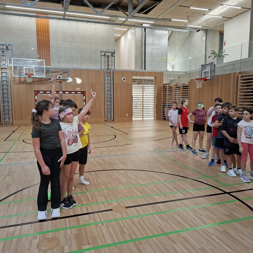 Eine Gruppe von Kindern steht auf einem Basketballplatz, wobei ein Mädchen nach oben zeigt.