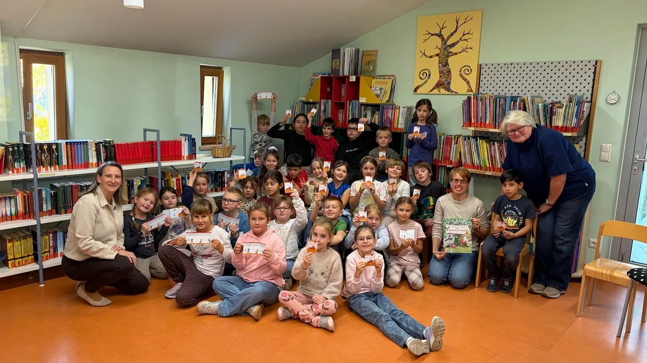 Eine Gruppe von Kindern und Erwachsenen posiert für ein Bild in einer Bibliothek. Sie halten Bücher und lächeln.