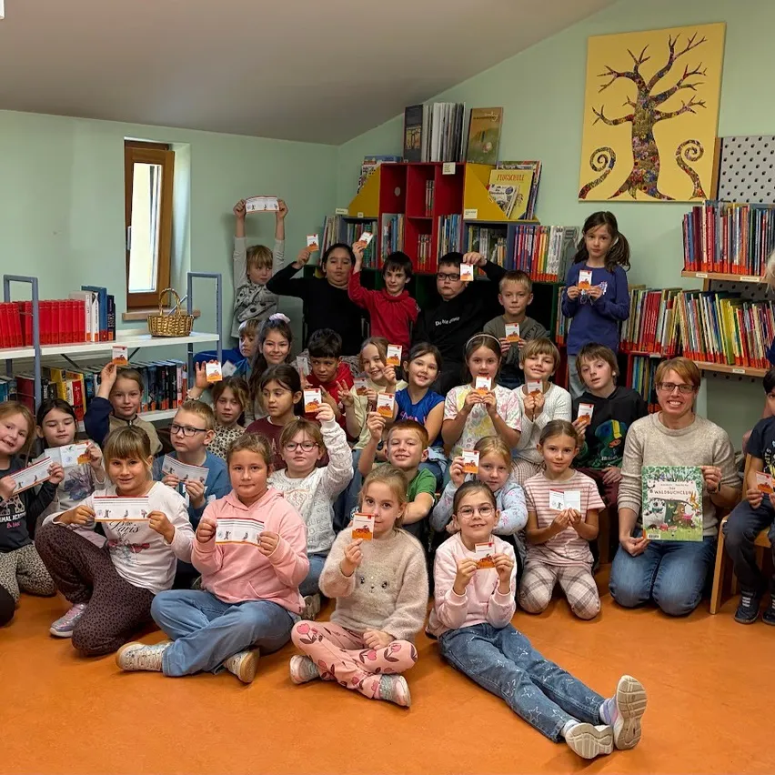 Eine Gruppe von Kindern und Erwachsenen posiert für ein Bild in einer Bibliothek. Sie halten Bücher und lächeln.