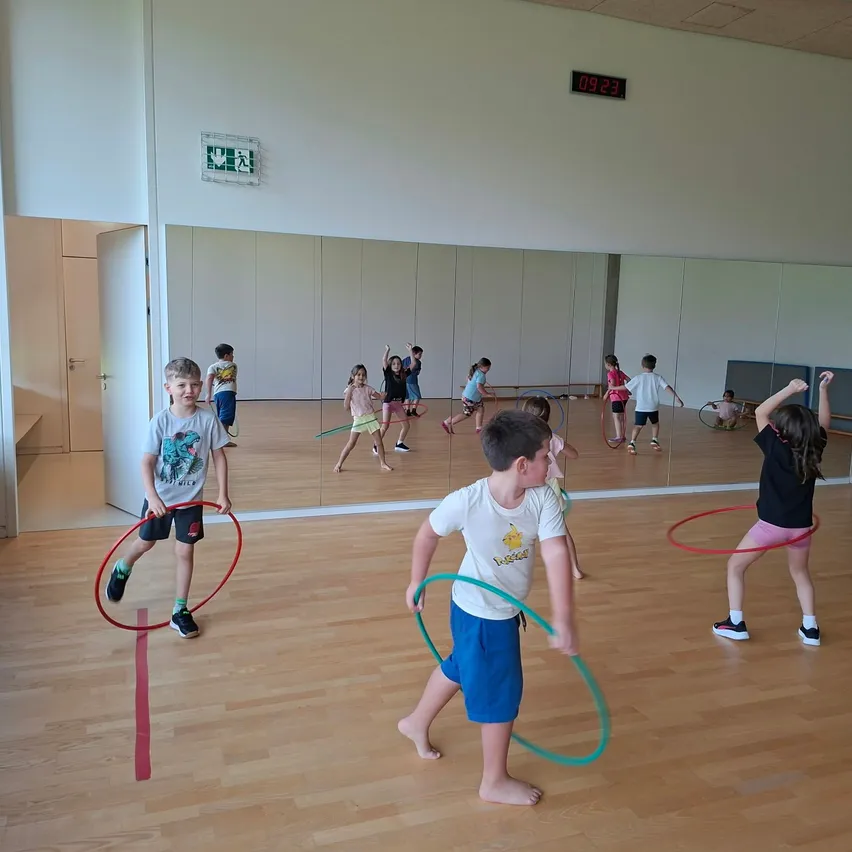 Eine Gruppe von Kindern spielt mit Hula-Hoops in einer Turnhalle.