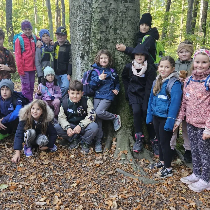 Eine Gruppe von Kindern in Winterkleidung posiert für ein Foto im Wald. Einige halten einen weißen Eimer, und einer steht auf einem Baumstamm.