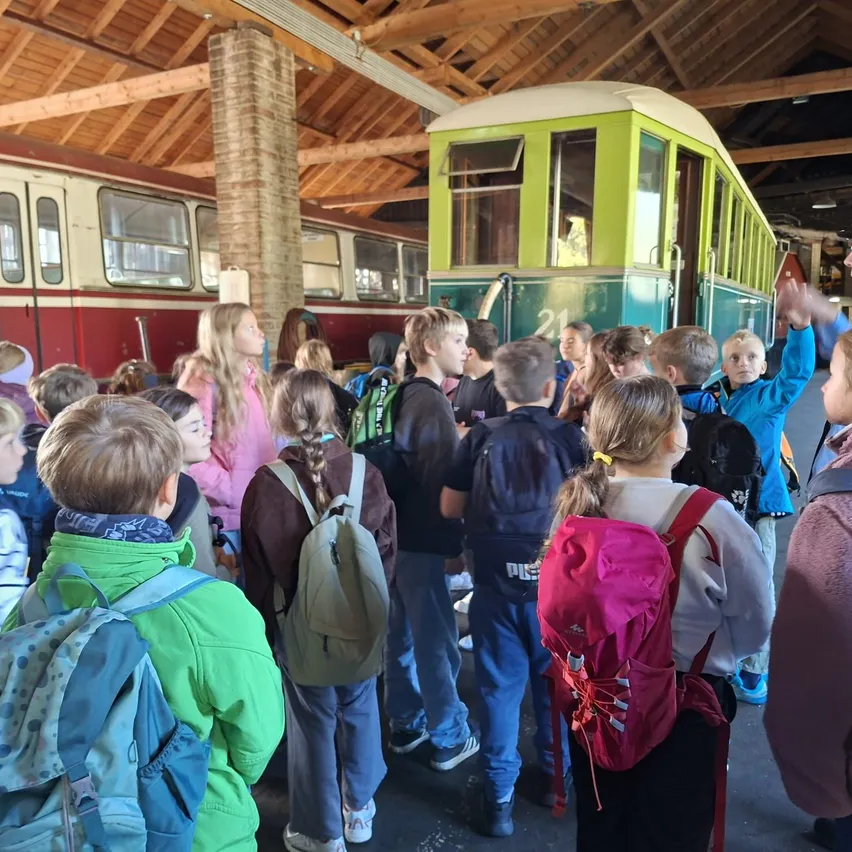 Eine Gruppe von Kindern und Erwachsenen versammelt sich um einen grünen und weißen Straßenbahn in einem Museum.