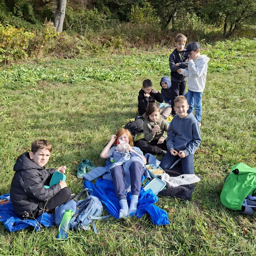 Eine Gruppe von Kindern sitzt auf einem Grasfeld, einige essen, während andere etwas betrachten.