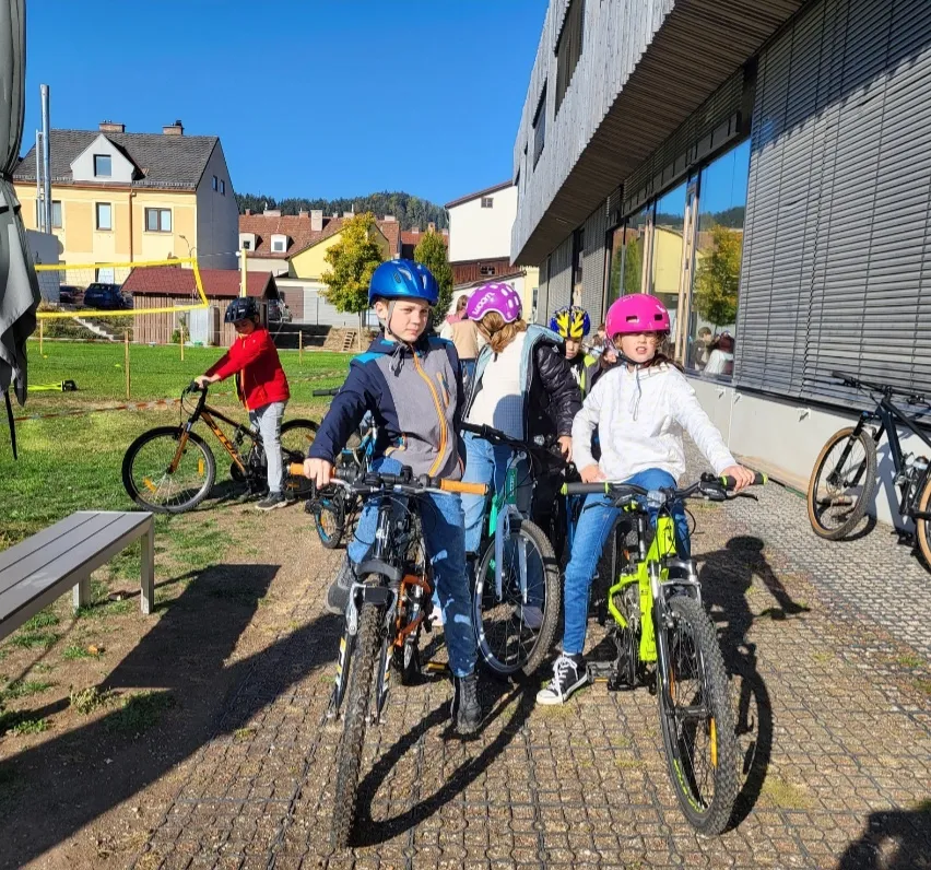 Eine Gruppe von Kindern in Helmen fährt mit ihren Fahrrädern vor einem Gebäude.