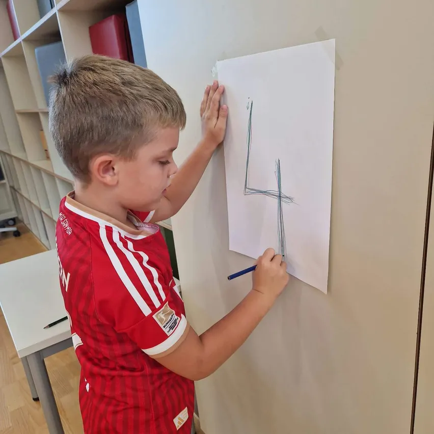 Ein kleiner Junge steht vor einer Wand und hält ein Stück Papier mit der Nummer vier darauf.