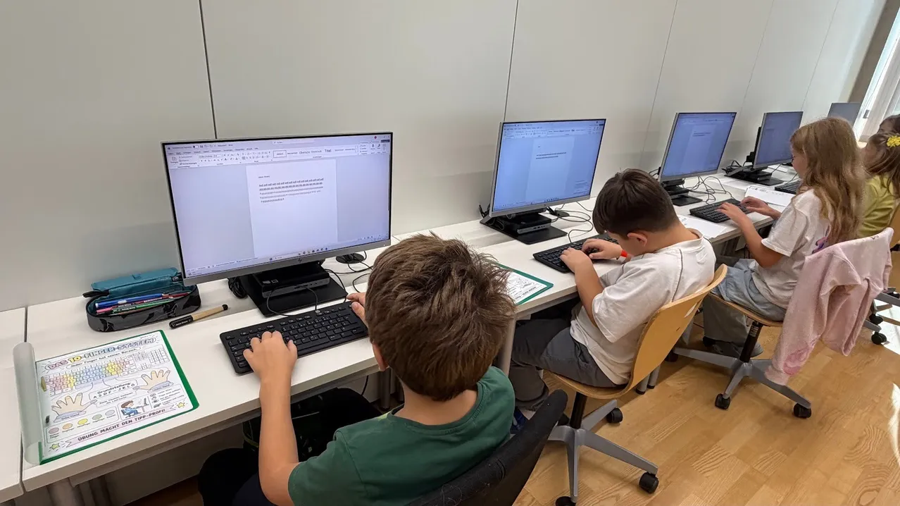 Vier Kinder sitzen an einem Schreibtisch mit Computern. Sie tippen auf ihren Tastaturen.